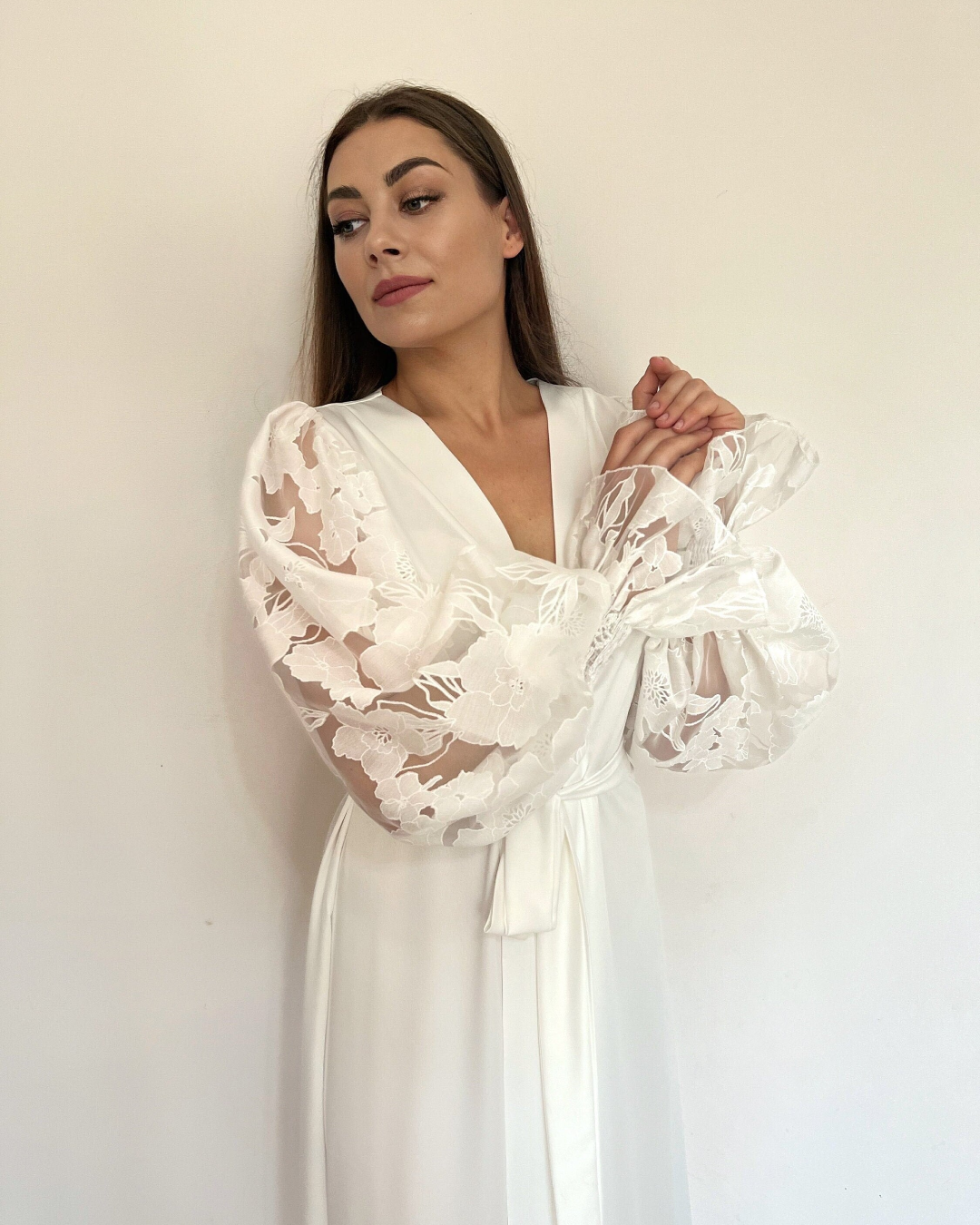 a bride in a white robe standing against a wall