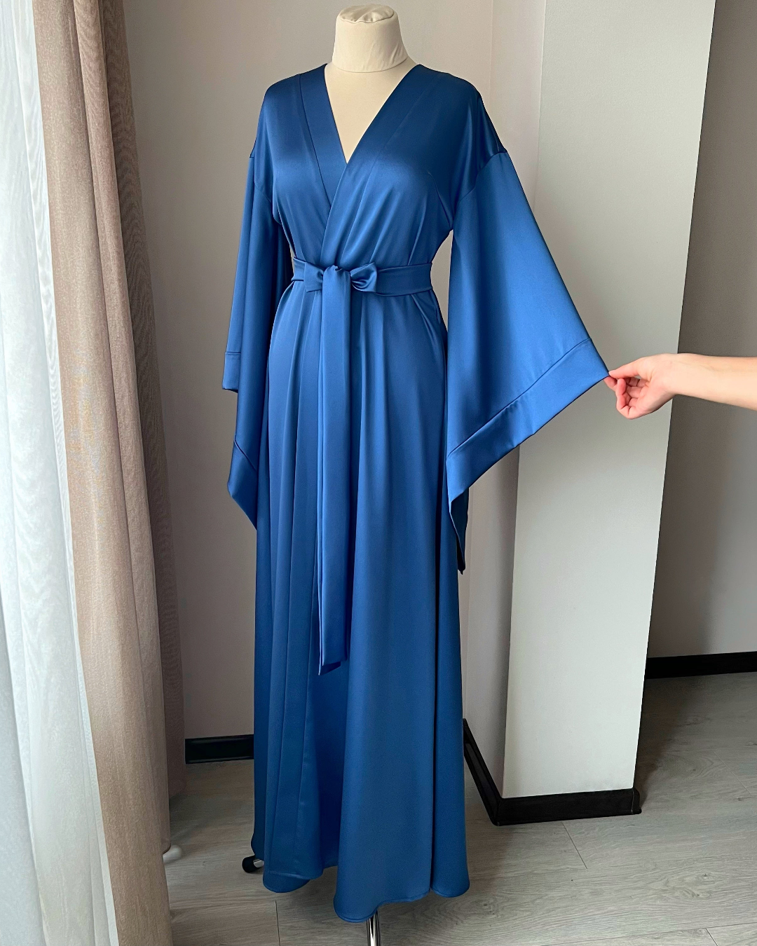 a woman's hand is pointing at a blue robe on a mannequin