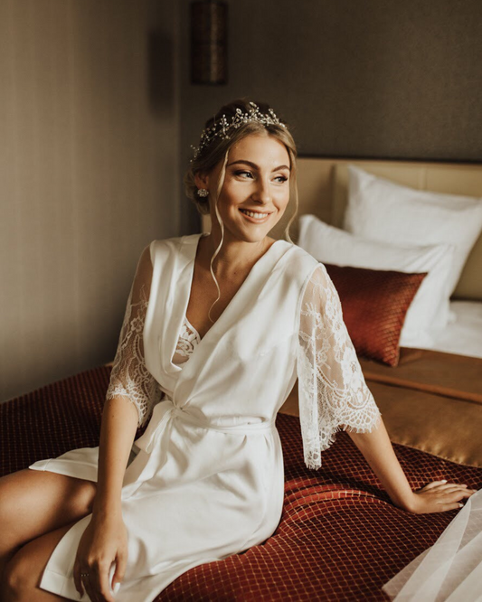a woman in a Bridal robe with lace sleeves sitting on a bed