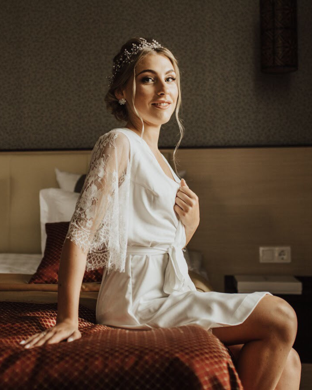 a woman in a Bridal robe with lace sleeves sitting on a bed